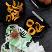 Cactus Tea Towel styled beside sliced peaches on a dark tabletop