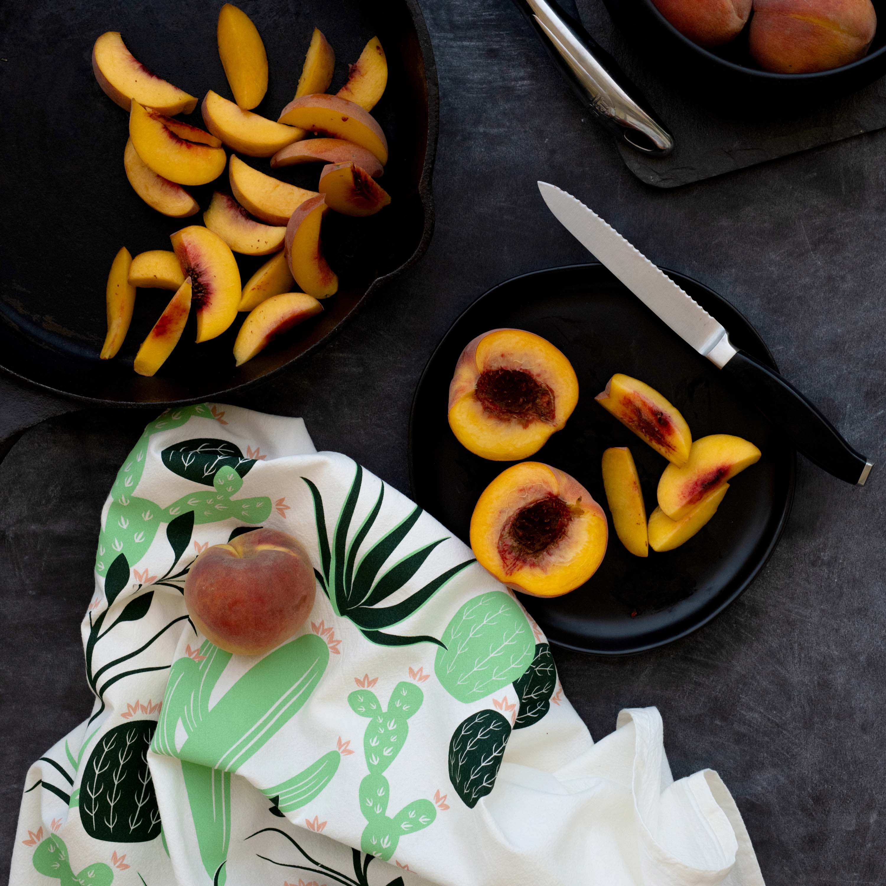 Cactus Tea Towel styled beside sliced peaches on a dark tabletop