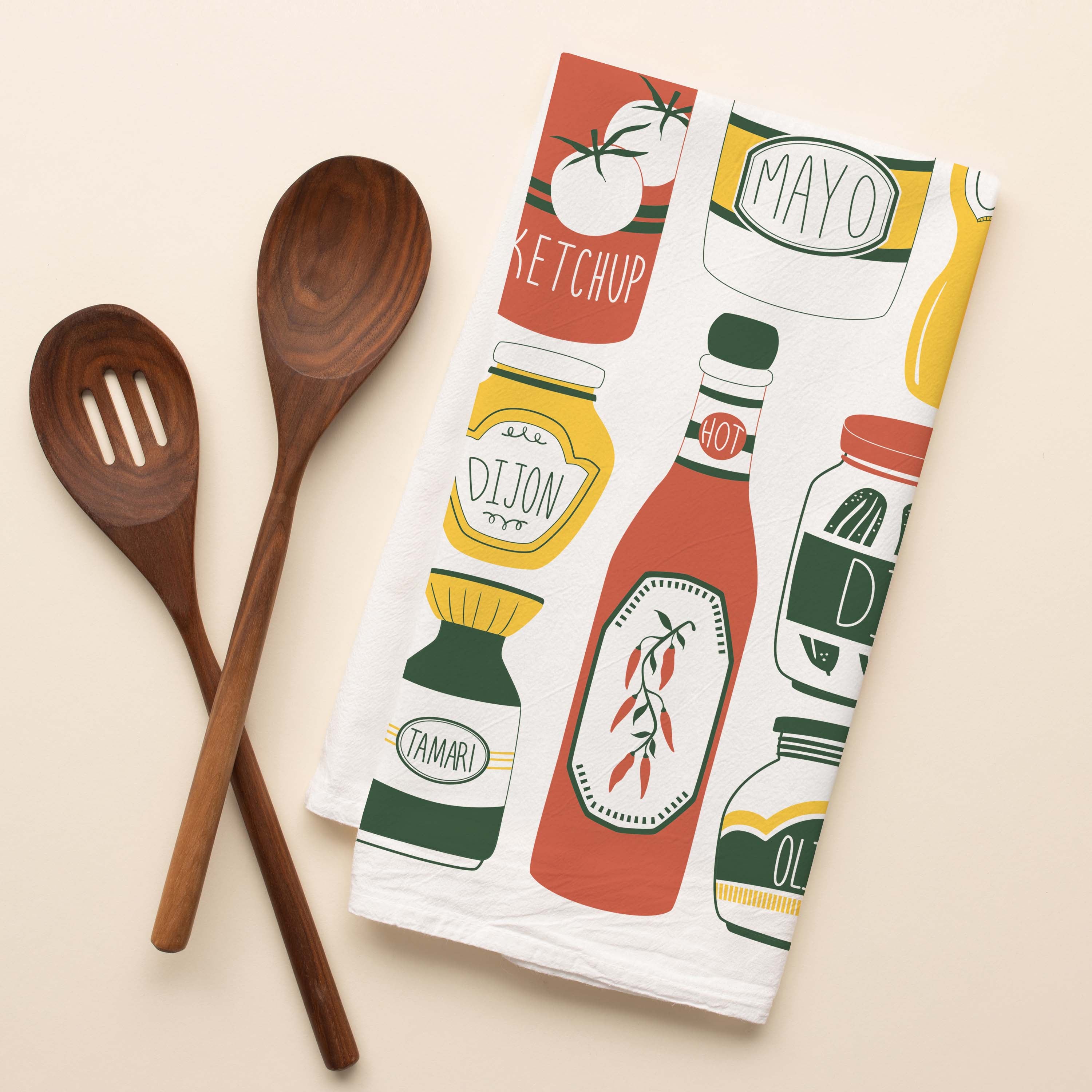 Classic Condiments Tea Towel with hand-illustrated condiment bottle and jar design beside wooden kitchen utensils