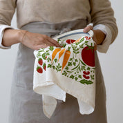 Person wearing an apron holding the Orange Farmers Market Tea Towel in both hands
