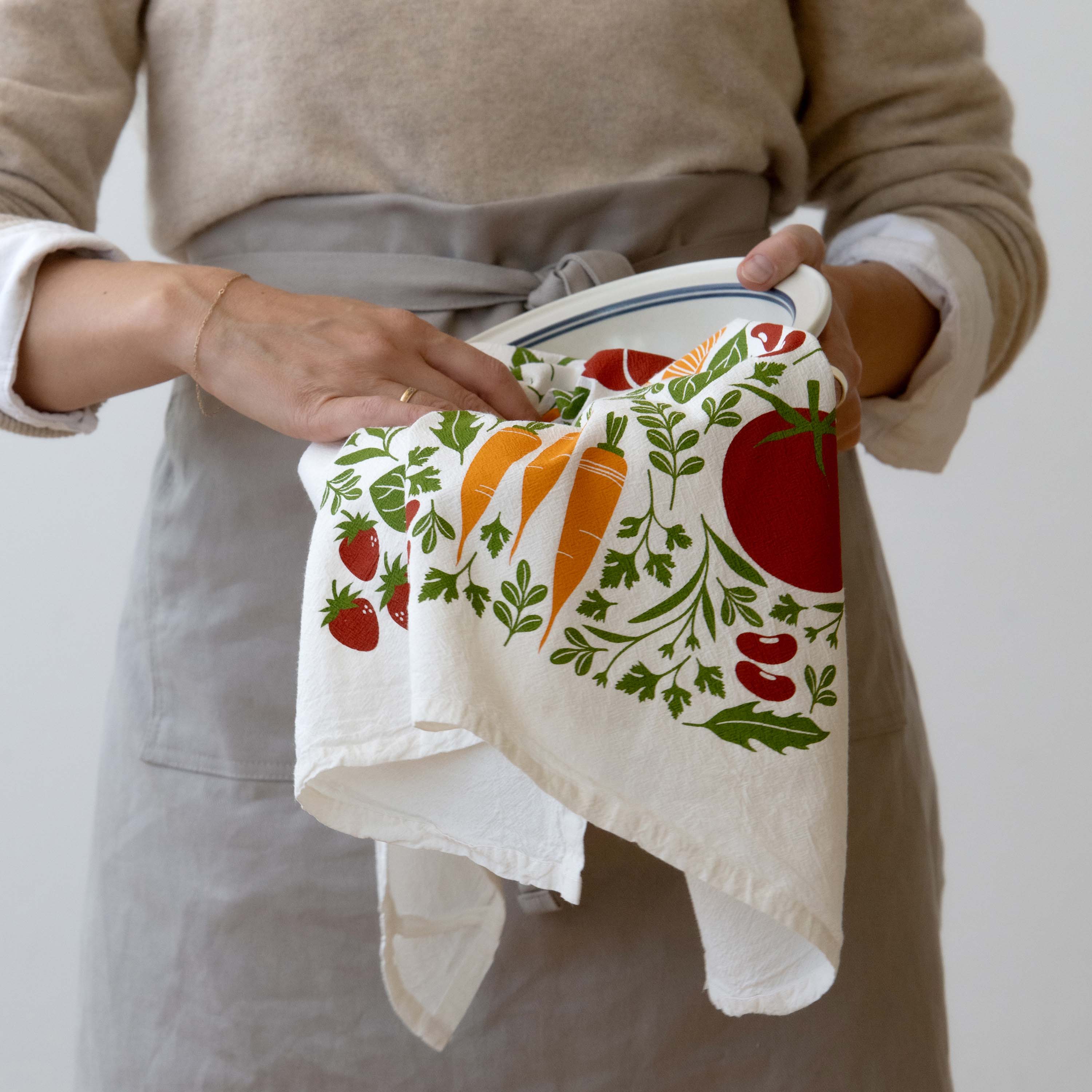 Person wearing an apron holding the Orange Farmers Market Tea Towel in both hands