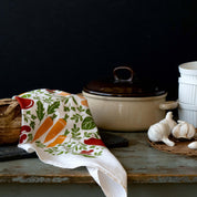 Orange Farmers Market Tea Towel draped beside a Dutch oven and garlic on a rustic table
