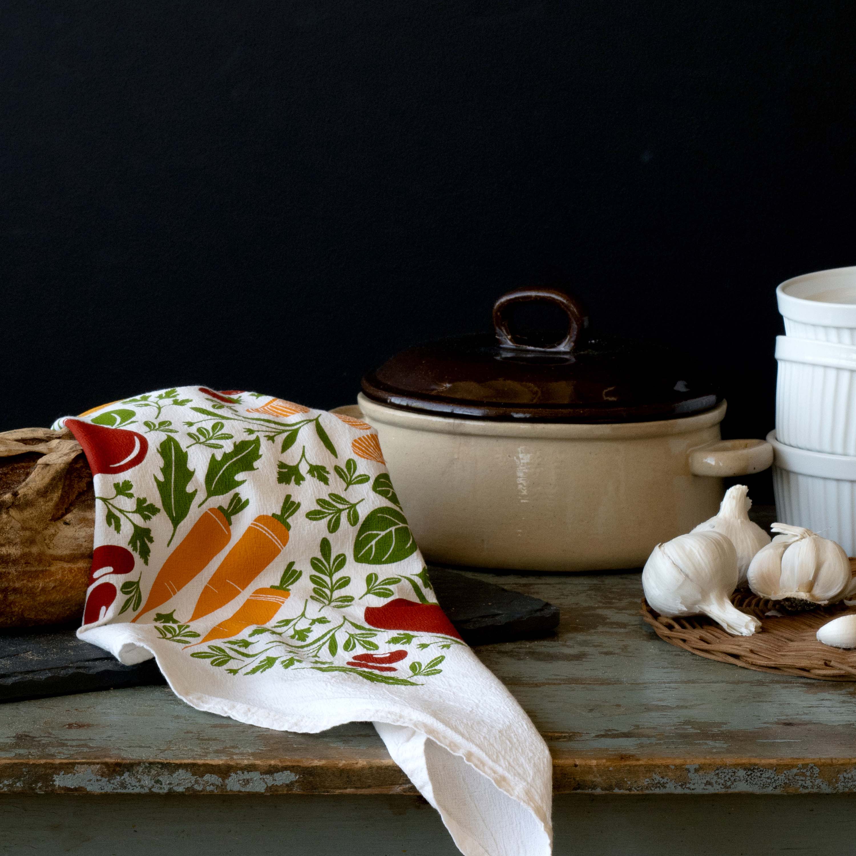 Orange Farmers Market Tea Towel draped beside a Dutch oven and garlic on a rustic table
