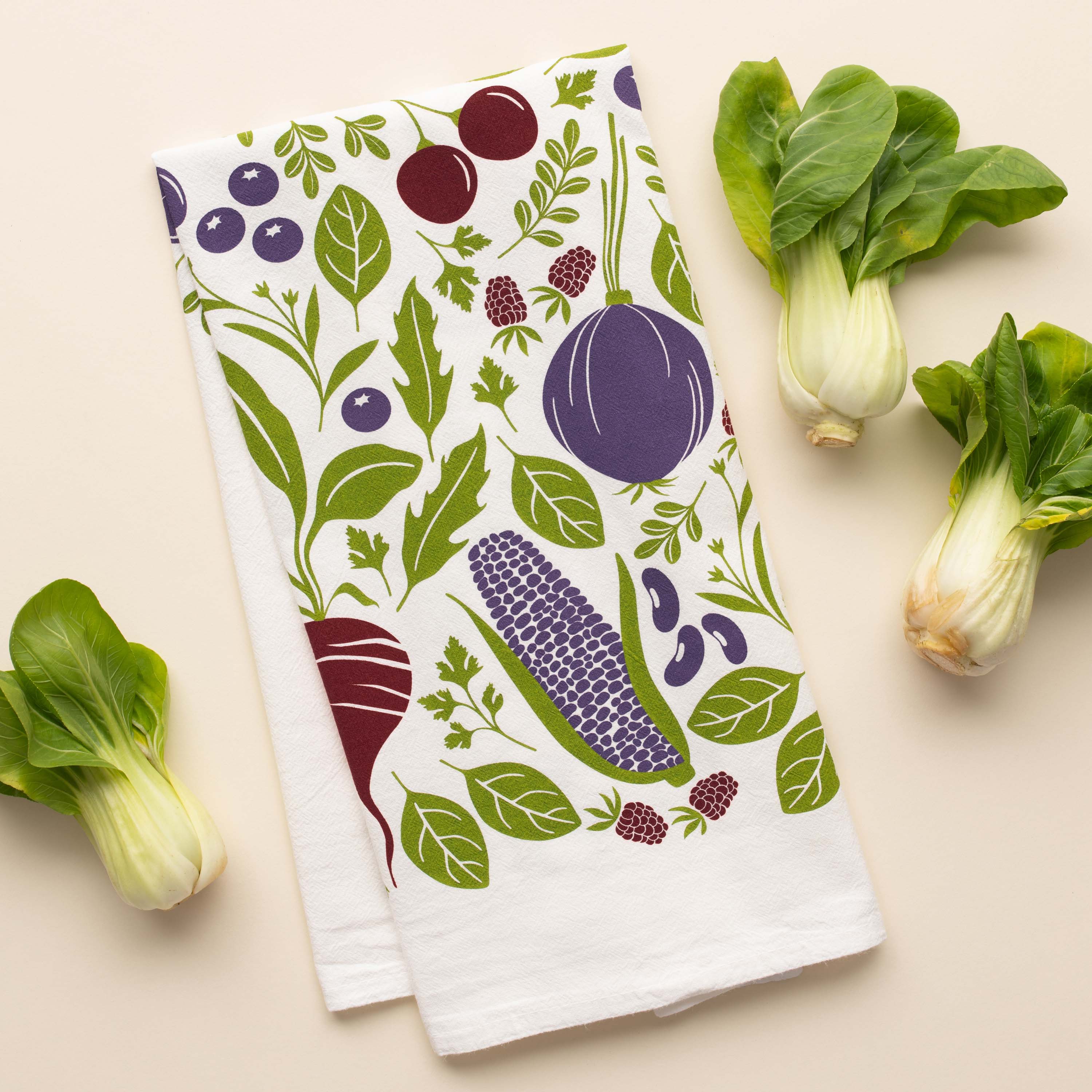Purple Farmers Market Tea Towel with hand-illustrated vegetable design beside fresh bok choy