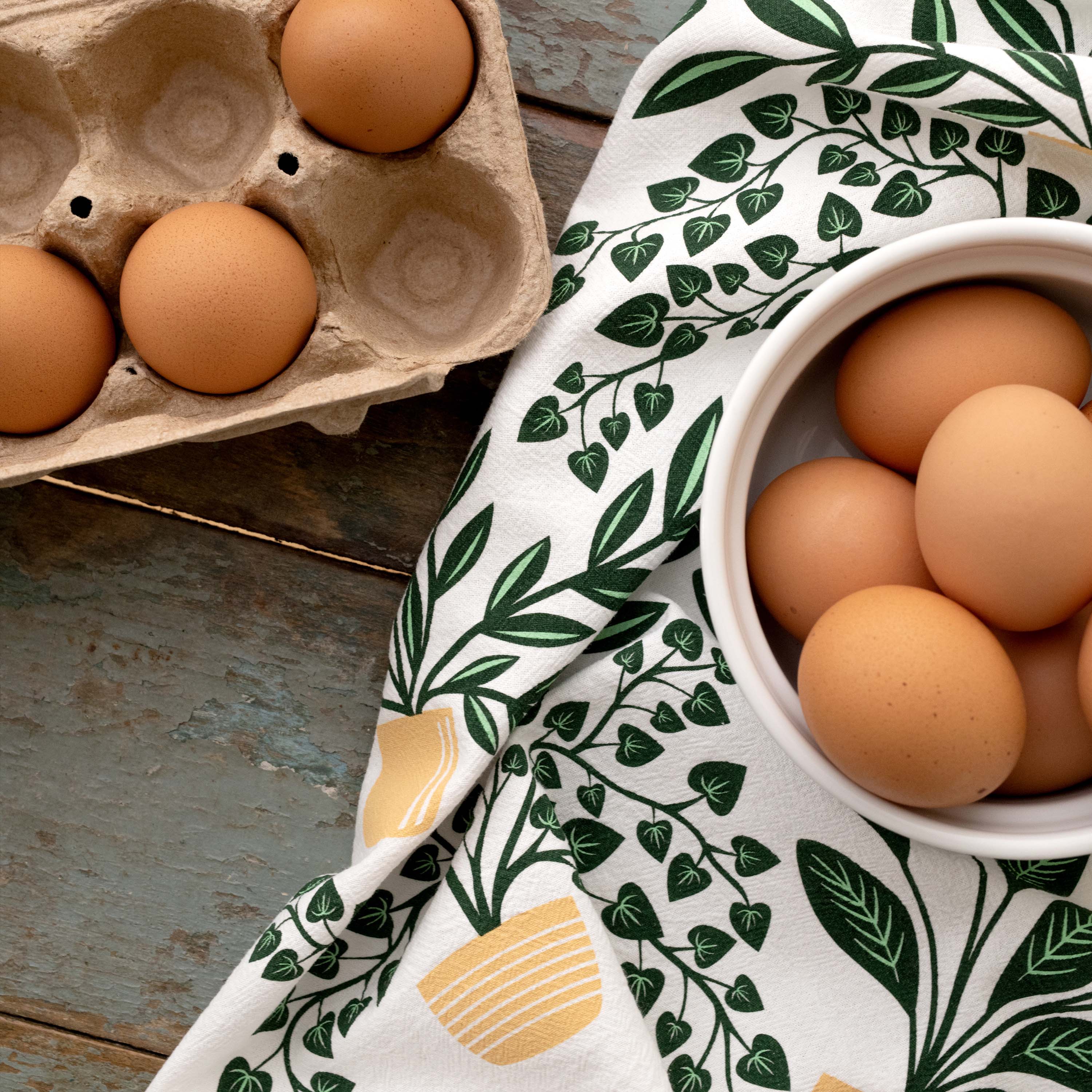 House Plants Tea Towel styled beside a bowl of brown eggs on a wooden table