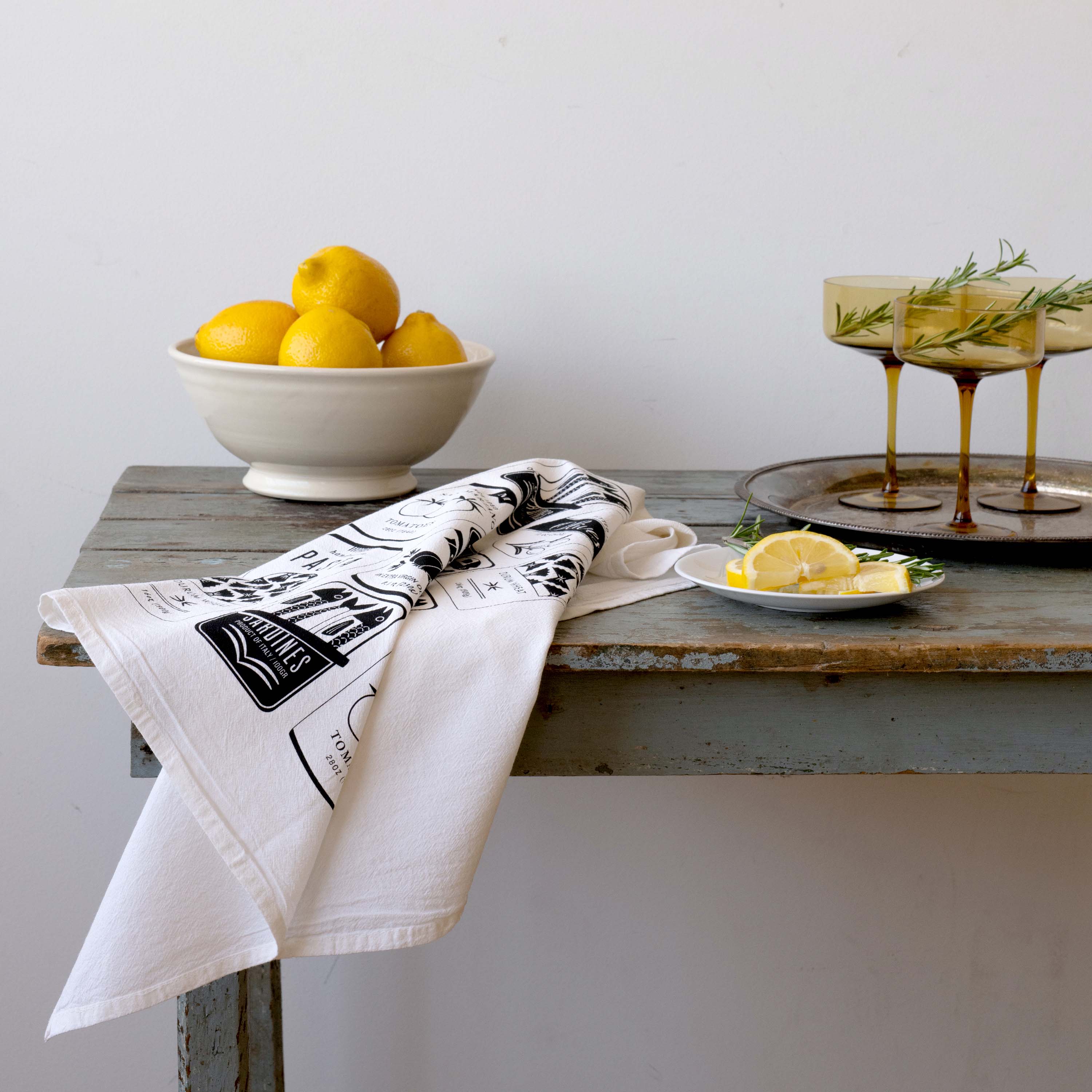 Italian Market Tea Towel draped over a wooden table beside lemons and drinks