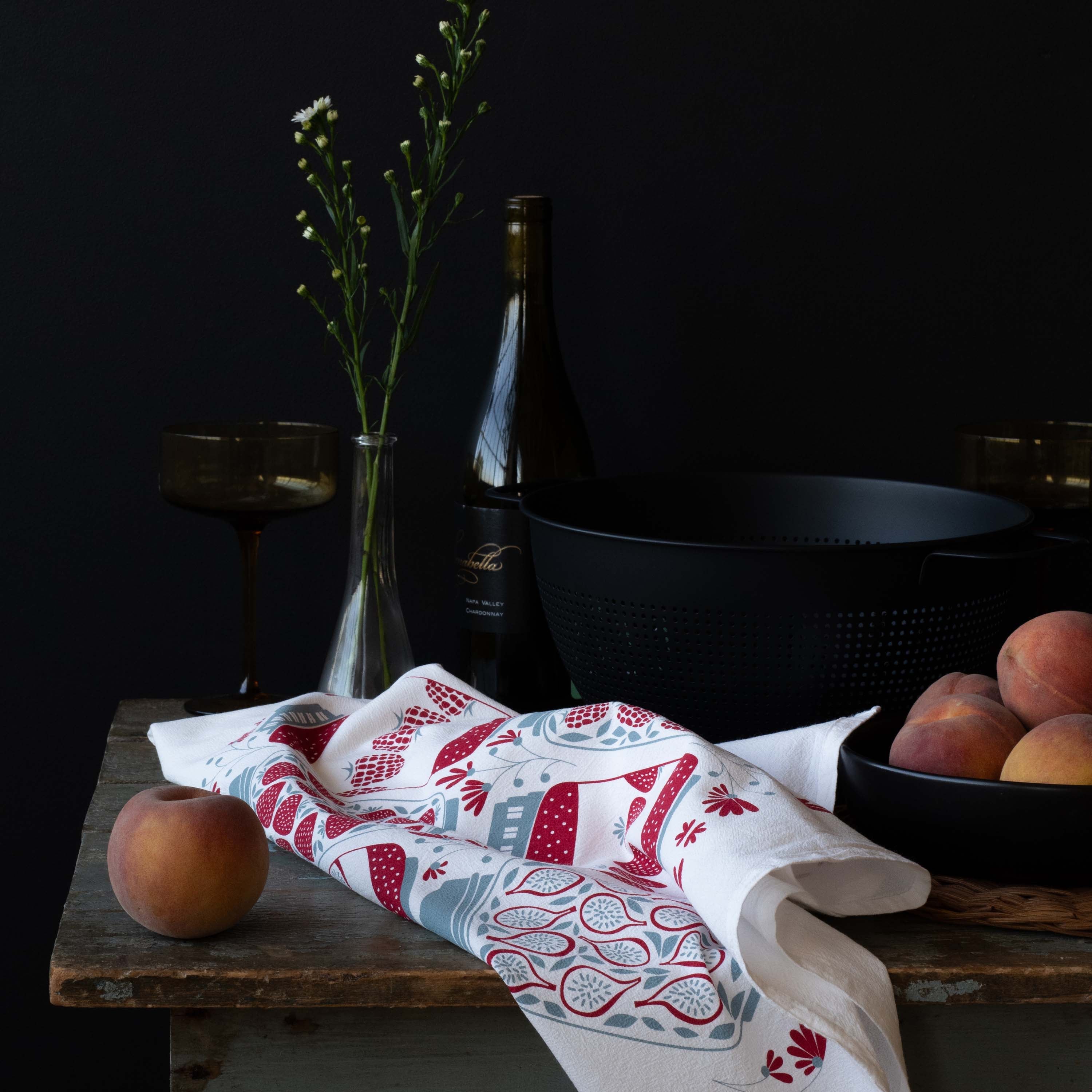 Jam Jars Tea Towel styled on a rustic table with peaches, glassware, and dark cookware