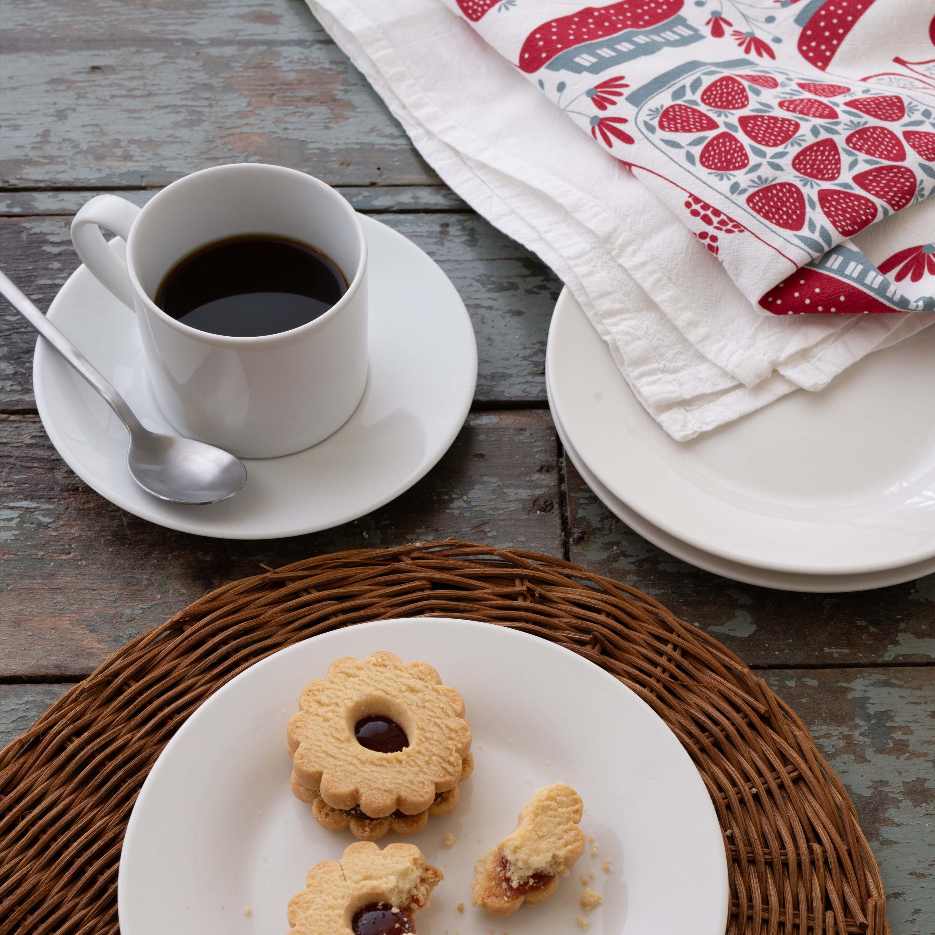 Jam Jars Tea Towel styled beside a coffee cup, plates, and cookies on a wooden table