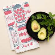 Jam Jars Tea Towel with hand-illustrated jam jar and strawberry design beside halved avocados and parsley