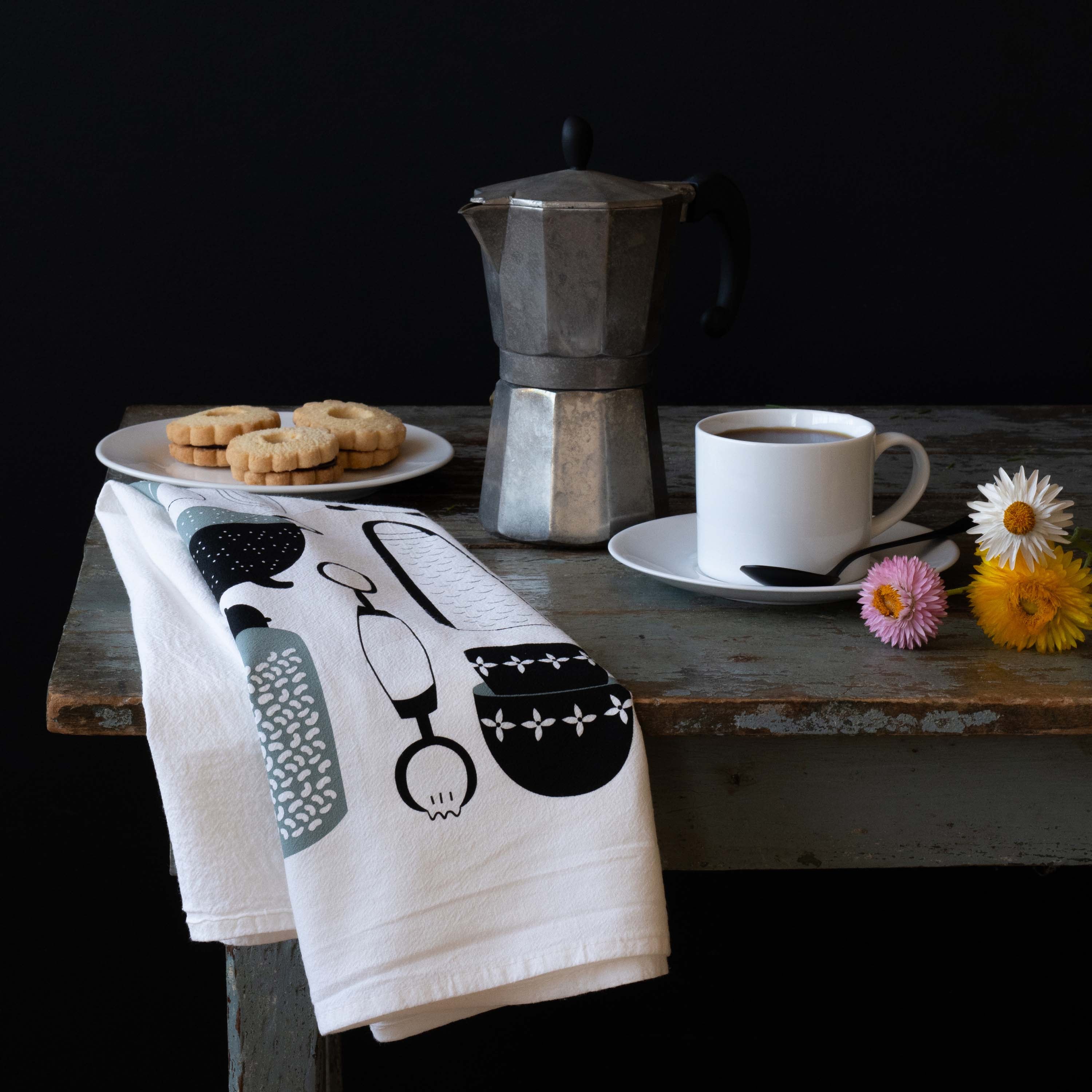 Kitchen Utensils Tea Towel styled with coffee, pastries, and small flowers on a rustic table