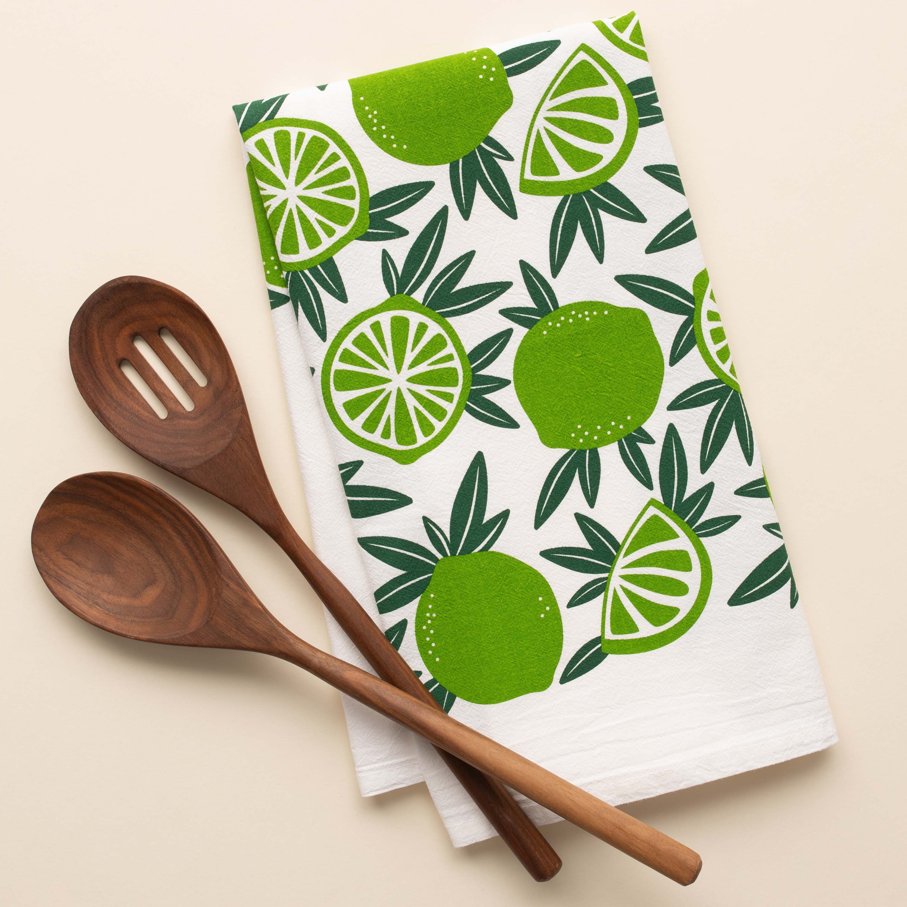 Limes Tea Towel with hand-illustrated lime design beside wooden kitchen utensils