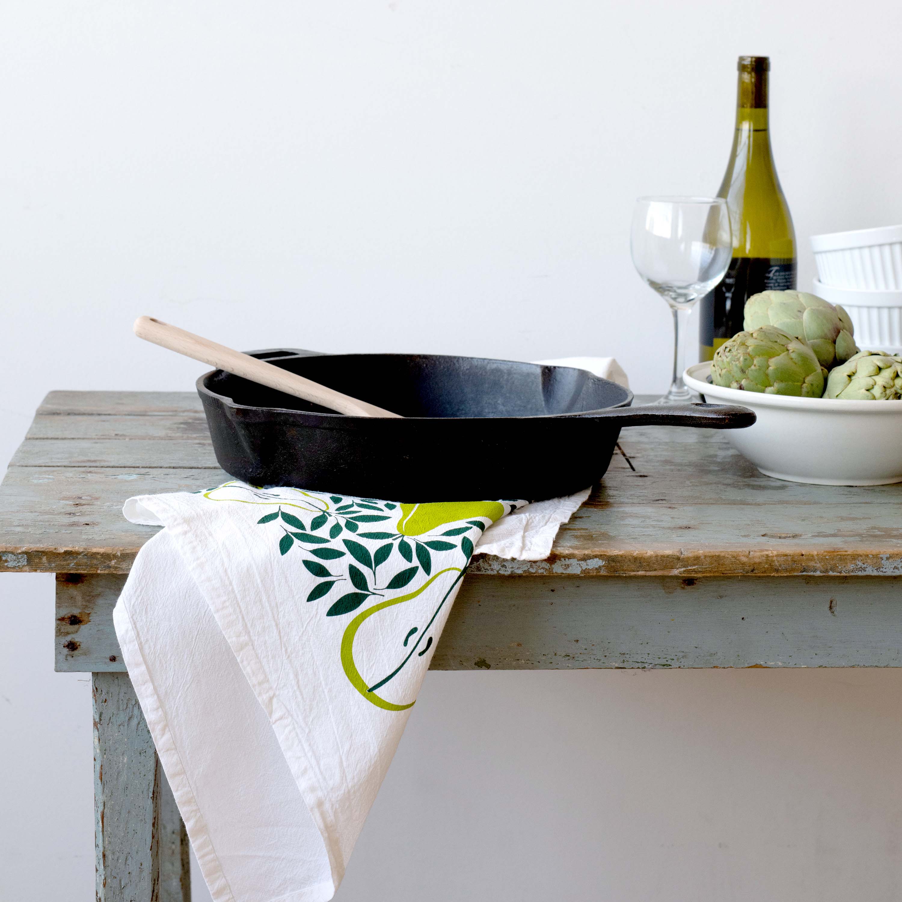 Pears Tea Towel draped over a kitchen counter beside a skillet, wine bottle, and artichoke