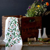 Wild Strawberries Tea Towel draped over a wooden crate with wildflowers, and glass vases