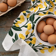 Sundrops Tea Towel draped beside a bowl of brown eggs on a wooden table