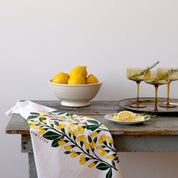 Sundrops Tea Towel styled on a wooden kitchen counter beside lemons and drinks