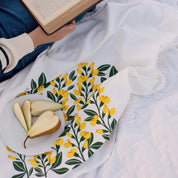 Sundrops Tea Towel styled on white picnic cloth with sliced pears and a person holding an open book