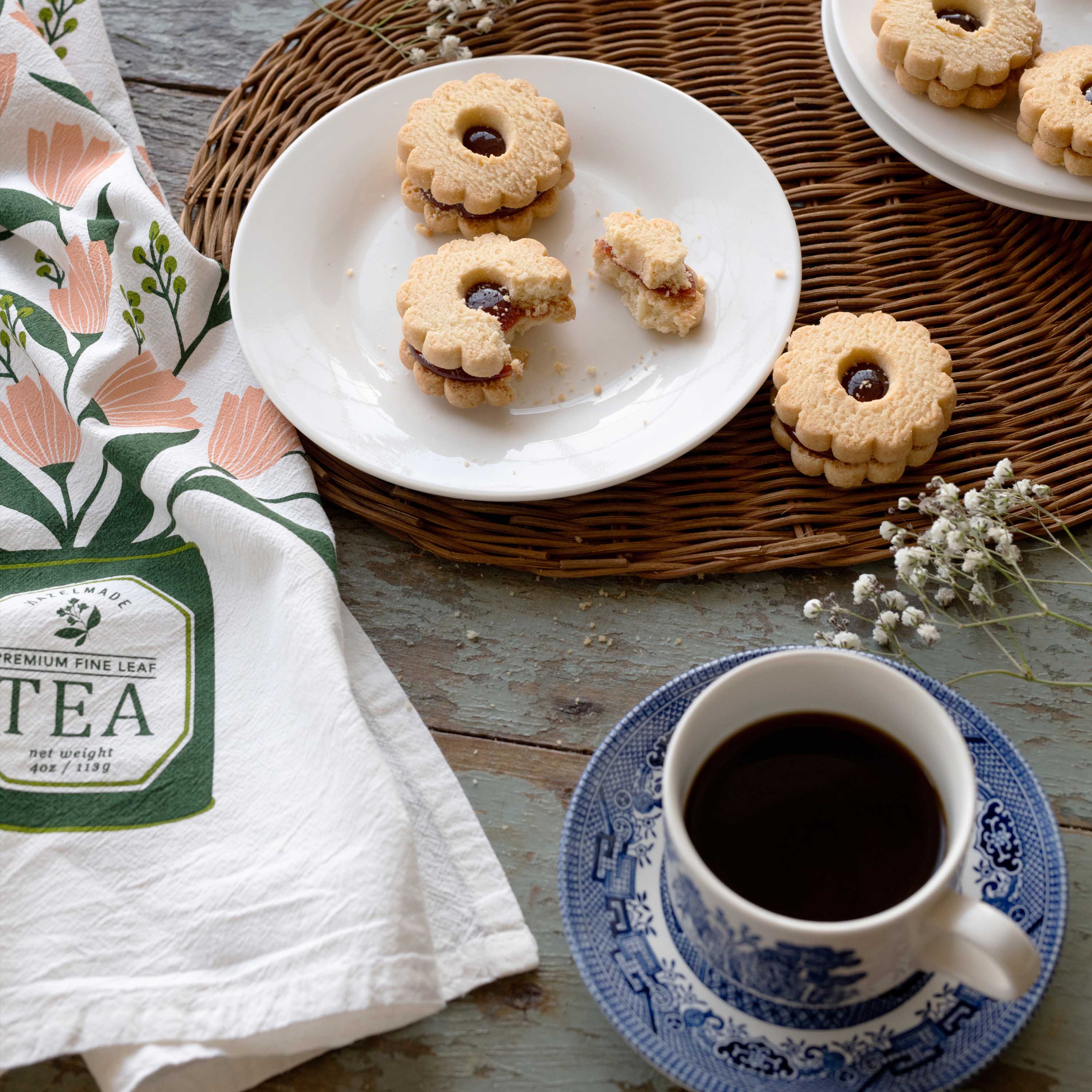 Hand-illustrated tea towel beside cookies and a cup of coffee on a rustic table