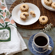 Tea Tin Bouquet Tea Towel styled beside a cup of tea and cookies on a tabletop