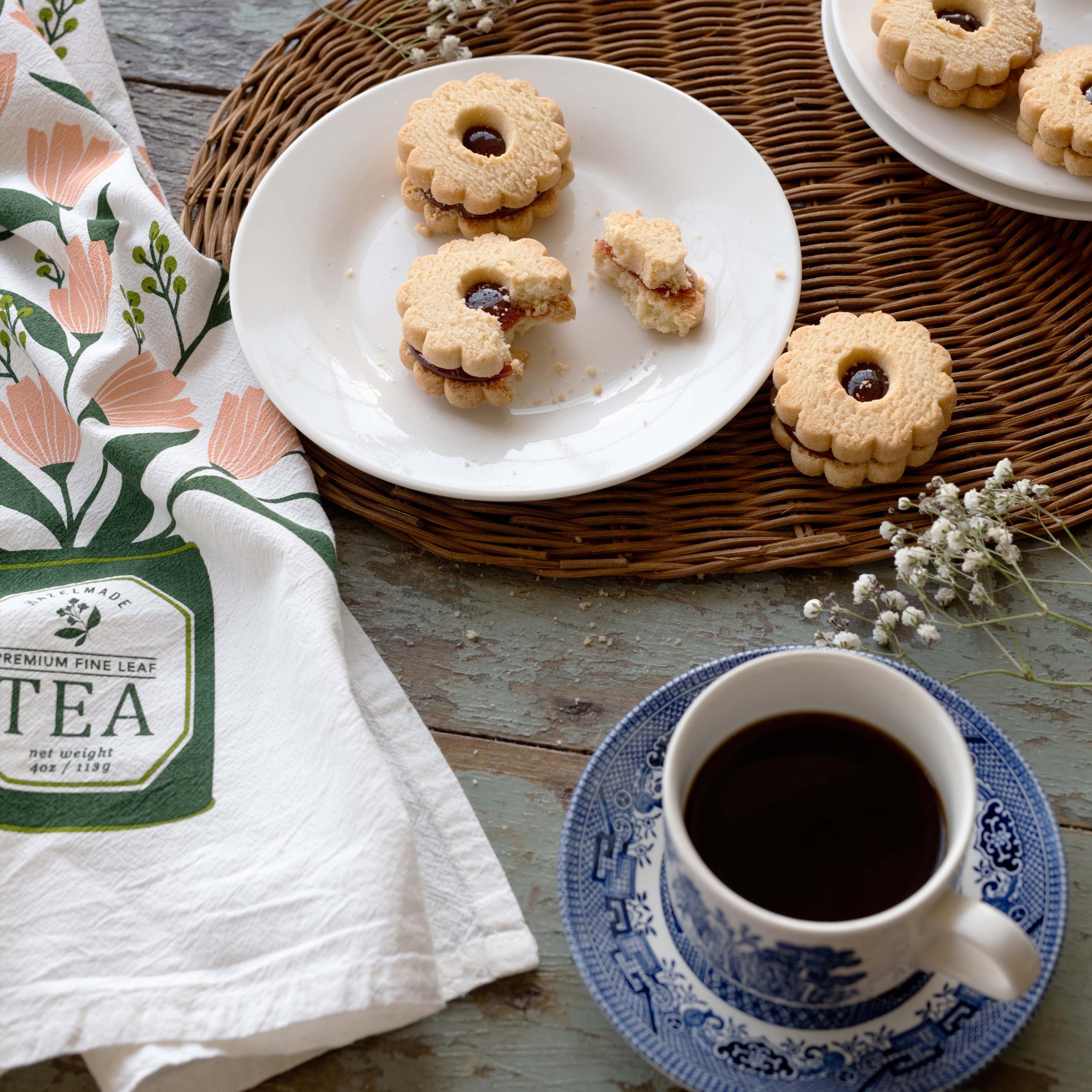 Tea Tin Bouquet Tea Towel styled beside a cup of tea and cookies on a tabletop