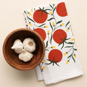 Tomatoes Tea Towel with hand-illustrated tomato design beside a wooden bowl of garlic