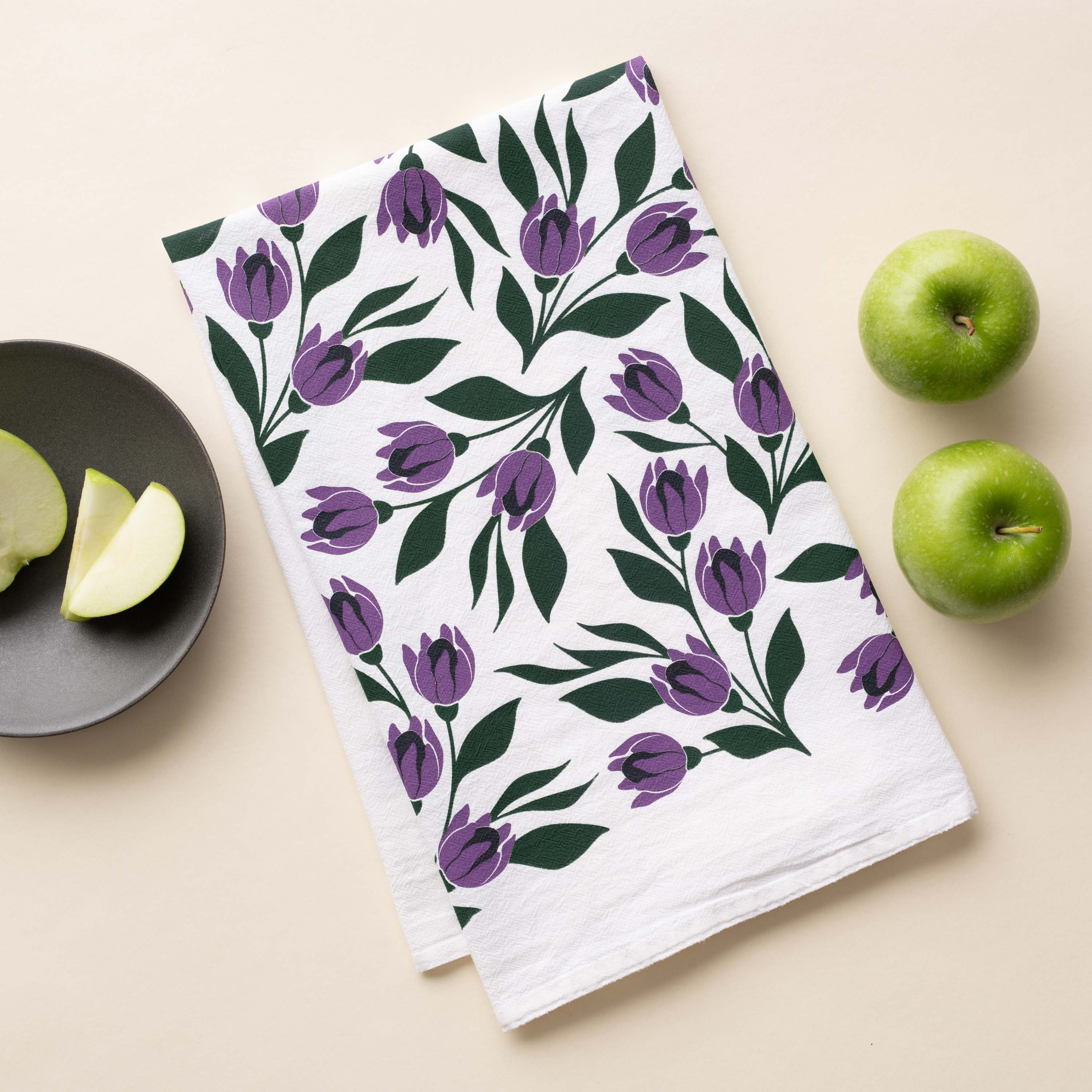 Tulips Tea Towel with hand-illustrated purple tulip design beside sliced green apples