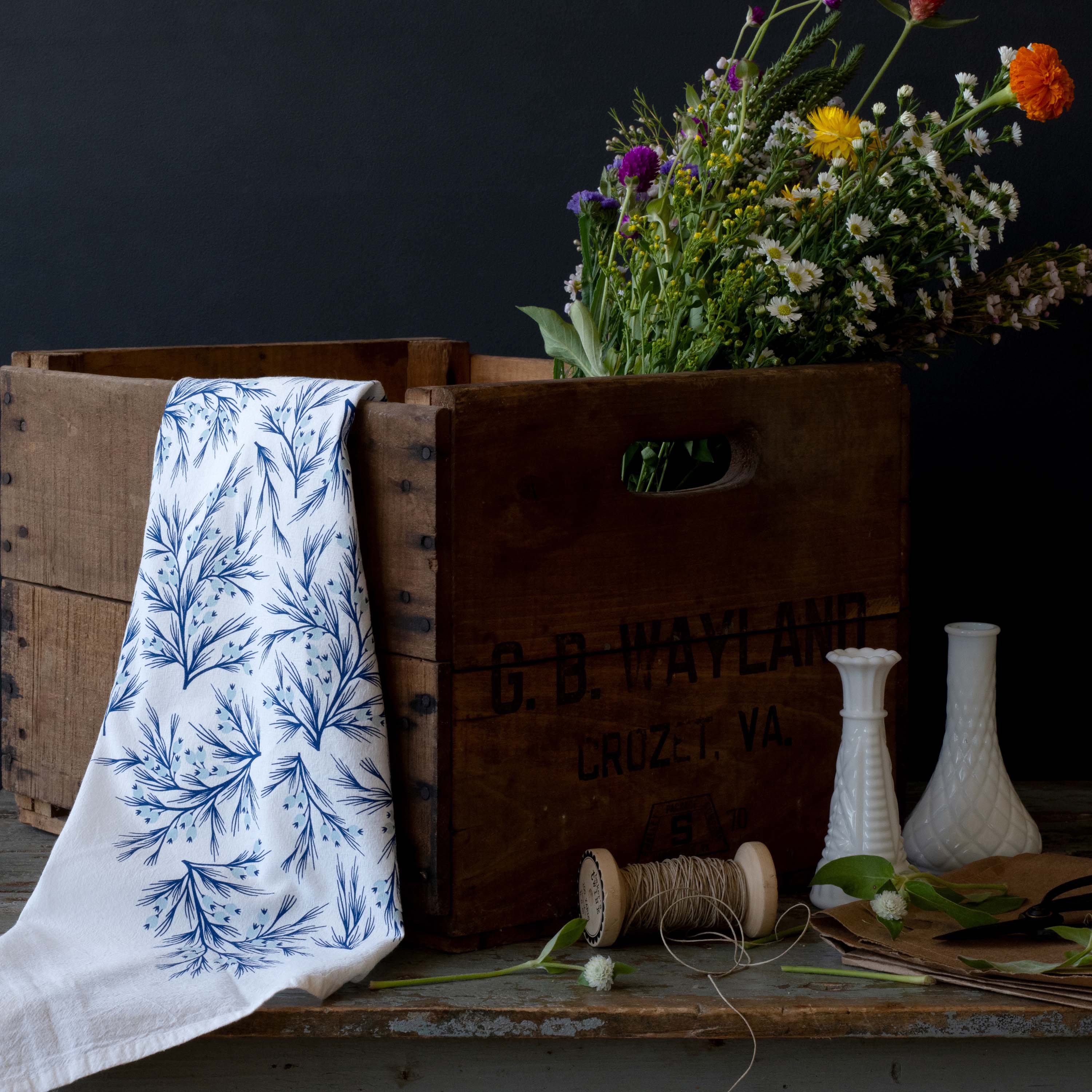 Winter Branch Tea Towel styled with a wooden crate, wildflowers, and glass vases