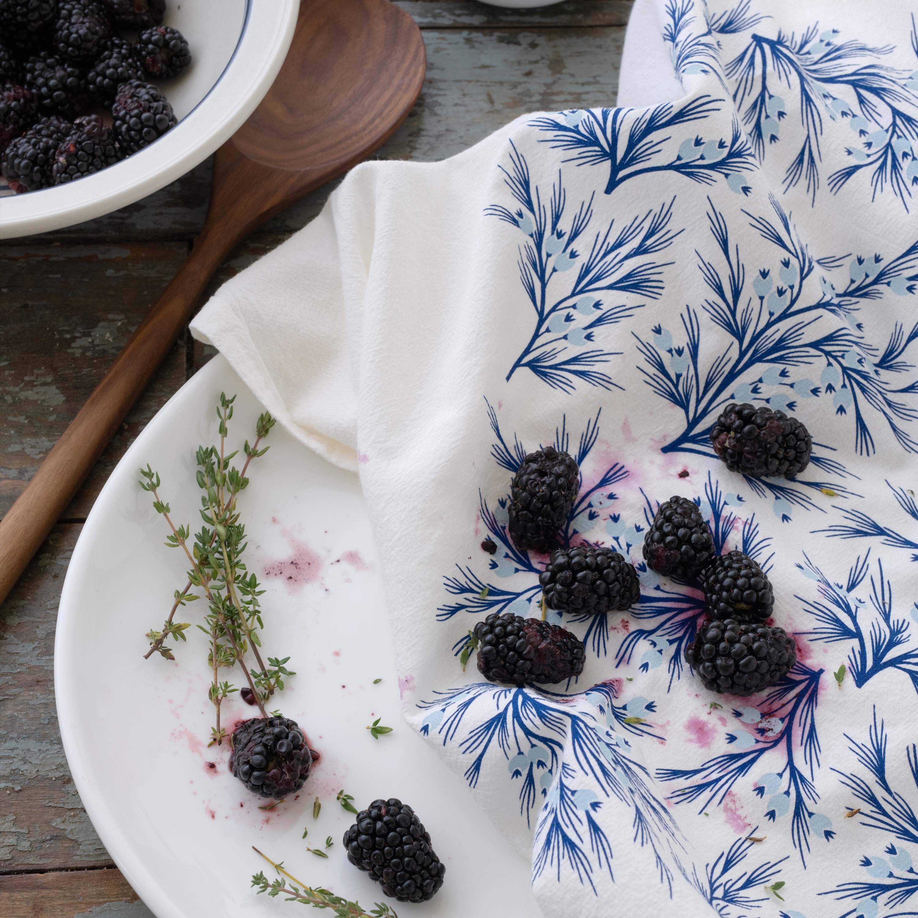 Winter Branch Tea Towel styled with blackberries and herbs on a wooden tabletop