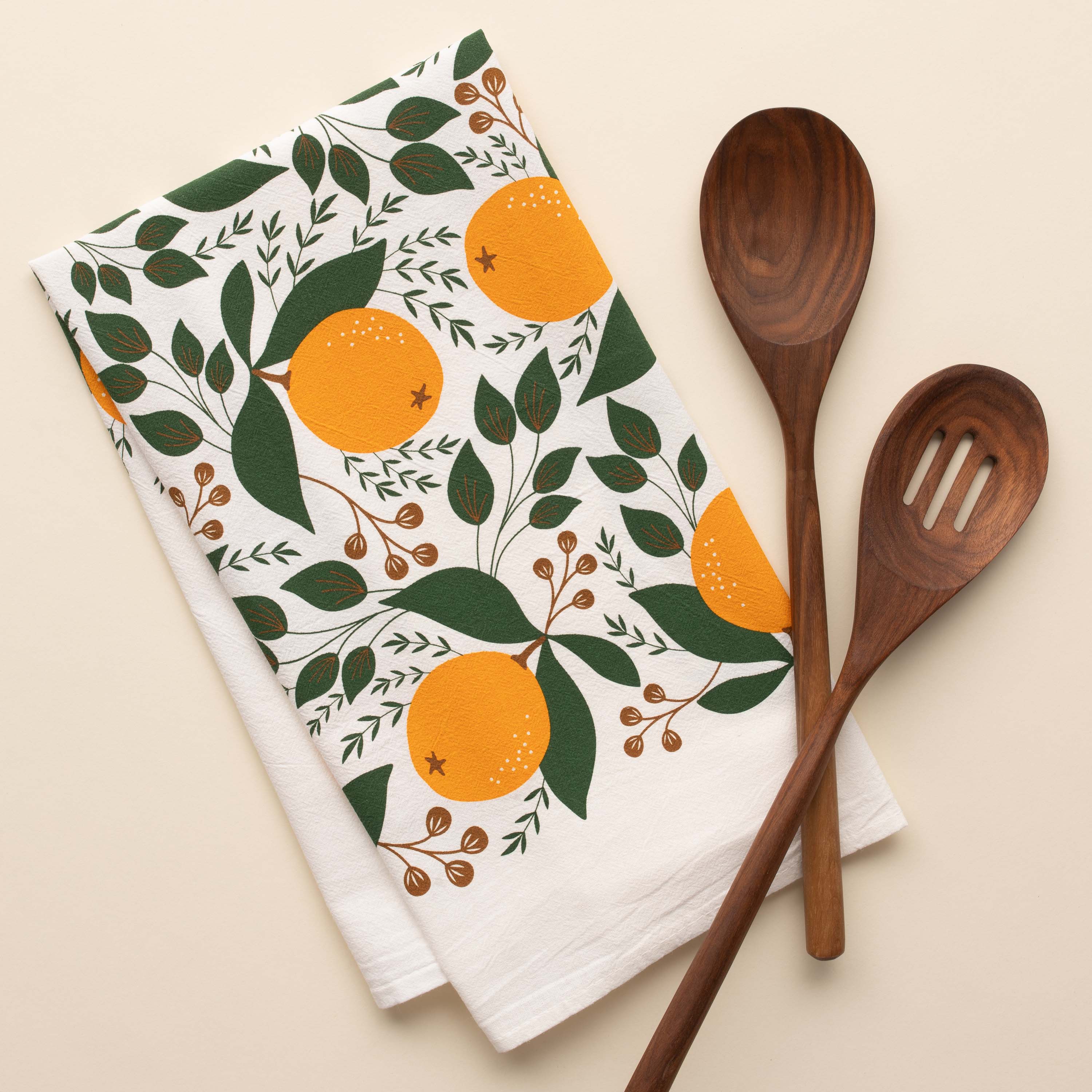 Winter Citrus Tea Towel with hand-illustrated citrus design beside wooden kitchen utensils