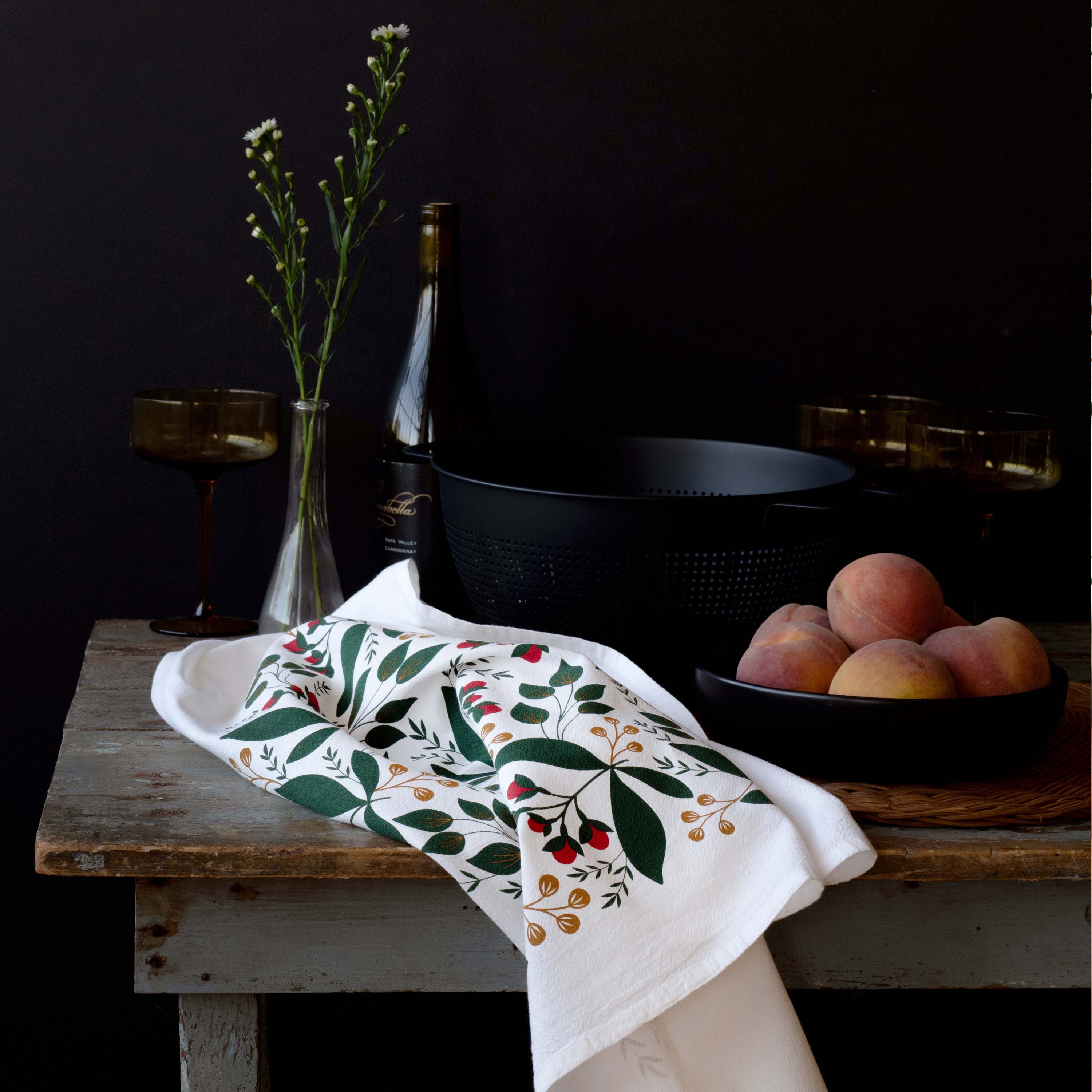 Winterberry Tea Towel styled on a rustic table with peaches, glassware, and dark cookware