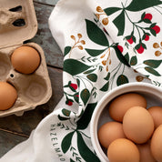 Winterberry Tea Towel styled beside a bowl of brown eggs on a wooden table