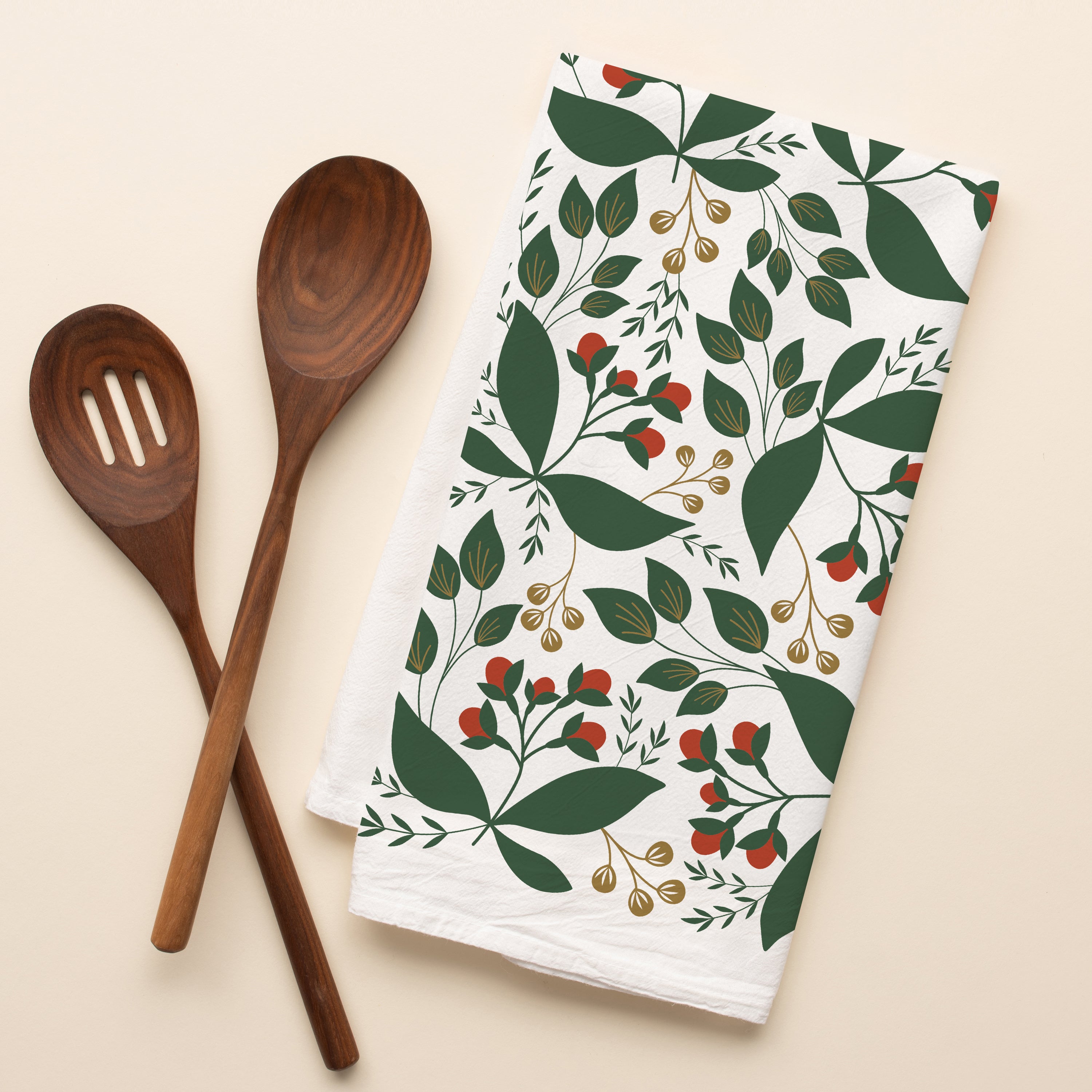 Winterberry Tea Towel with hand-illustrated winterberry design beside wooden kitchen utensils