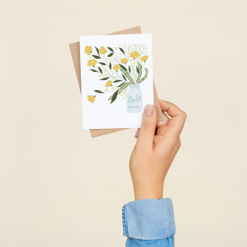 Single folded A2 greeting card with an envelope with an illustration of a mason jar with yellow flowers and green leaves coming out of it.