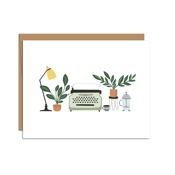 Single folded A2 greeting card with an envelope with an illustration of a lamp, plant, typewriter, and various other desk items in the center of the card.