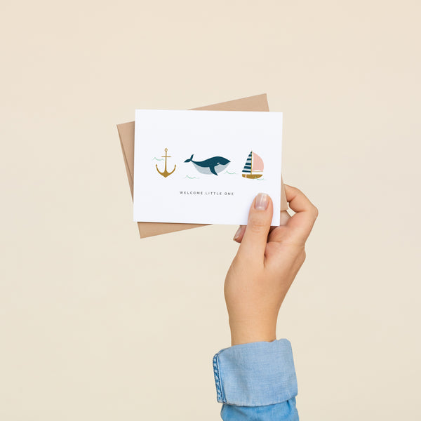 Single folded A2 greeting card with an envelope with an illustration of an anchor, whale, and boat with text below all three stating "Welcome Little One".