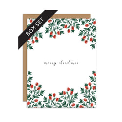 Box set of 8 folded A2 greeting cards with envelopes with an illustration  of red holly berries and green leaves bordering the top and bottom of the card. In the center of the card is text in cursive that states "Merry Christmas".