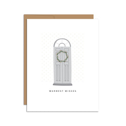 Single folded A2 greeting card with an envelope with an illustration of a gray door with a wreath and directly below it is text that states "Warmest Wishes".