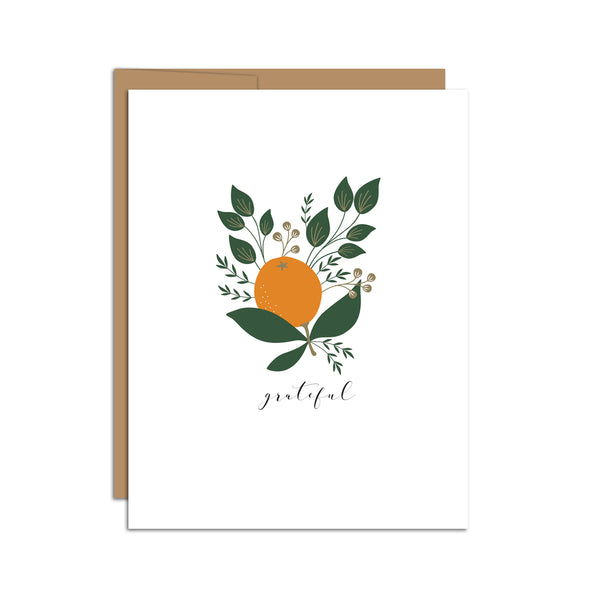 Single folded A2 greeting card with an envelope with an illustration of a singular orange with green leaves around it. Directly below the orange is text in cursive that states "Grateful".