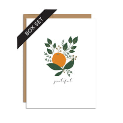 Box set of 8 folded A2 greeting cards with envelopes with an illustration  of a singular orange with green leaves around it. Directly below the orange is text in cursive that states "Grateful".
