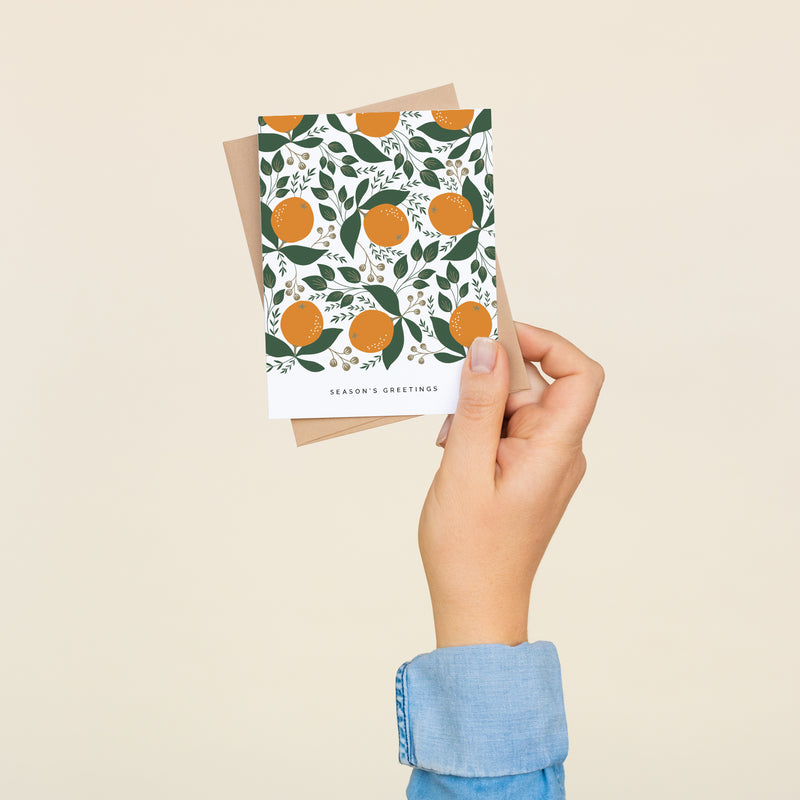 Box set of 8 folded A2 greeting cards with envelopes with an illustration  of oranges and green leaves in a repeating pattern. Below is text that states "Season's Greetings".