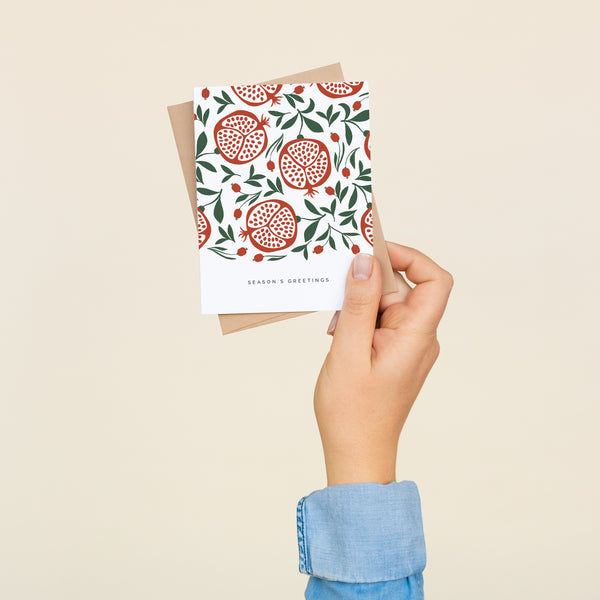 Box set of 8 folded A2 greeting cards with envelopes with an illustration  of a pattern of pomegranates open with seeds and below the pattern is text that states "Season's Greetings".
