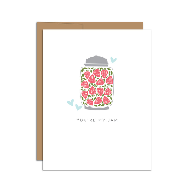 Single folded A2 greeting card with an envelope with an illustration of a jar filled with strawberries and a few blue hearts surrounding the jar. Directly below the jar is text that states "You're My Jam".