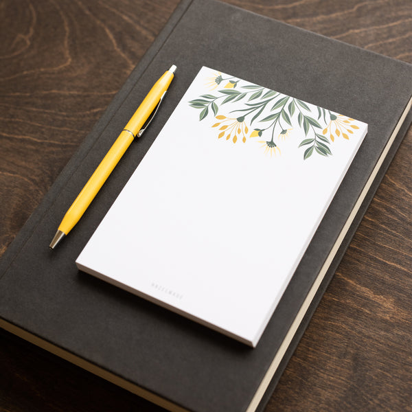 A single 4” by 5.5” small notepad with 50 tear-off sheets and an illustration of yellow flowers and green leaves sprouting from the top of the notepad while the rest is blank.