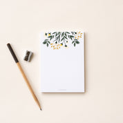 A single 4” by 5.5” small notepad with 50 tear-off sheets and an illustration of yellow flowers and green leaves sprouting from the top of the notepad while the rest is blank.
