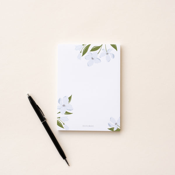 A single 4” by 5.5” small notepad with 50 tear-off sheets and an illustration of blue dogwood flowers coming from the top of the notepad as well as both the bottom left and right corners. The rest is blank.