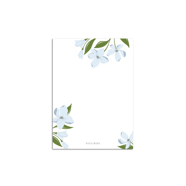 A single 4” by 5.5” small notepad with 50 tear-off sheets and an illustration of blue dogwood flowers coming from the top of the notepad as well as both the bottom left and right corners. The rest is blank.