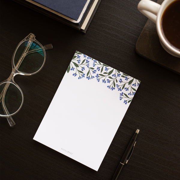 A single 4” by 5.5” small notepad with 50 tear-off sheets and an illustration of small blue flowers and green leaves wrapping the top of the notepad and the rest being blank.