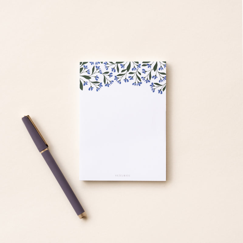 A single 4” by 5.5” small notepad with 50 tear-off sheets and an illustration of small blue flowers and green leaves wrapping the top of the notepad and the rest being blank.