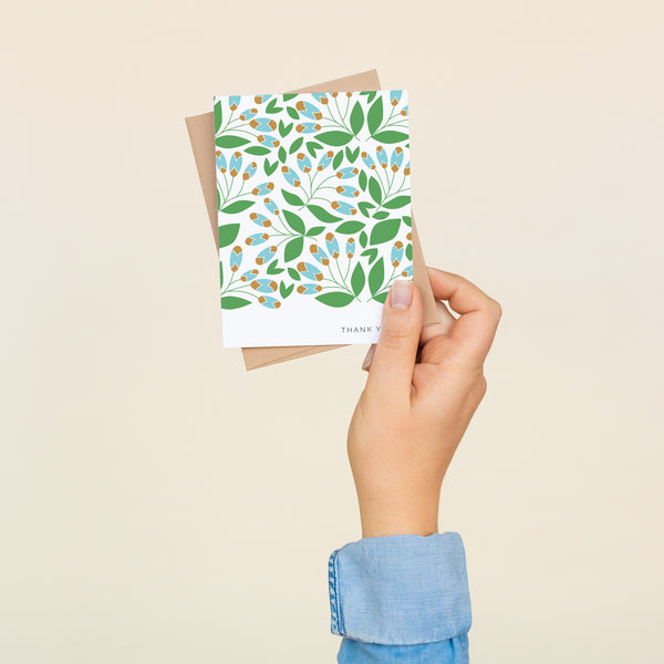 Box set of 8 folded A2 greeting cards with envelopes with an illustration  of green leaves and blue and brown detail branching off of the leaves. In the bottom right is text that states "Thank You".