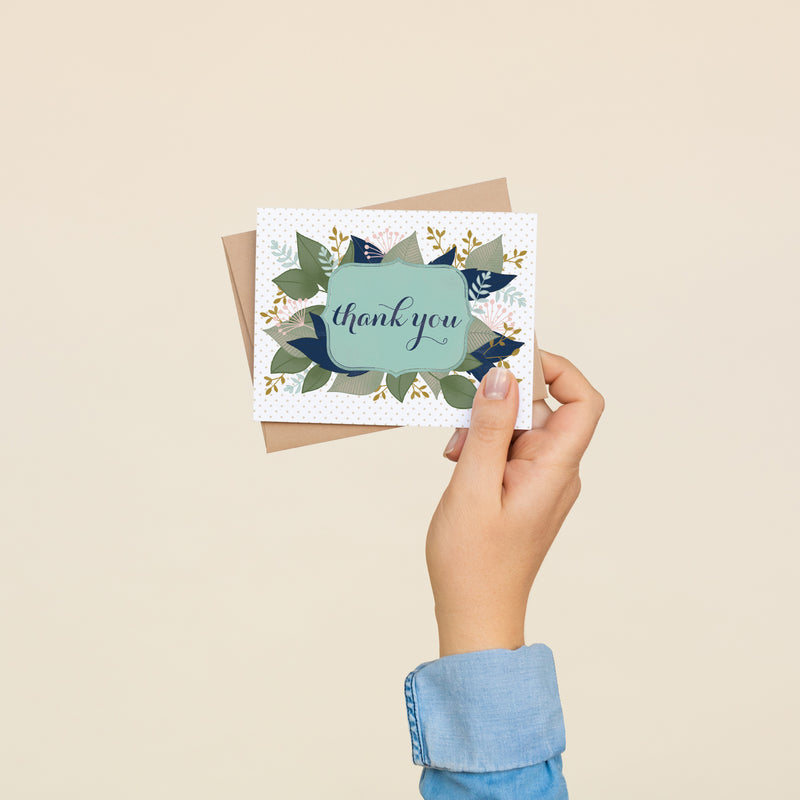 Box set of 8 folded A2 greeting cards with envelopes with an illustration    of text stating "Thank You" in cursive bordered by a blue background and leaves sprouting behind it.