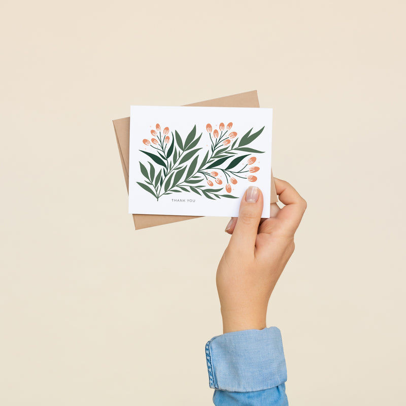 Single folded A2 greeting card with an envelope with an illustration of a green branch with leaves and orange seeds. Text below the branch states "Thank You".
